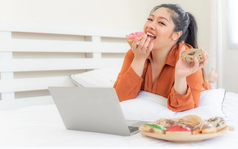 Ilustrasi perempuan makan sambil nonton yang bisa membuat berat badan naik