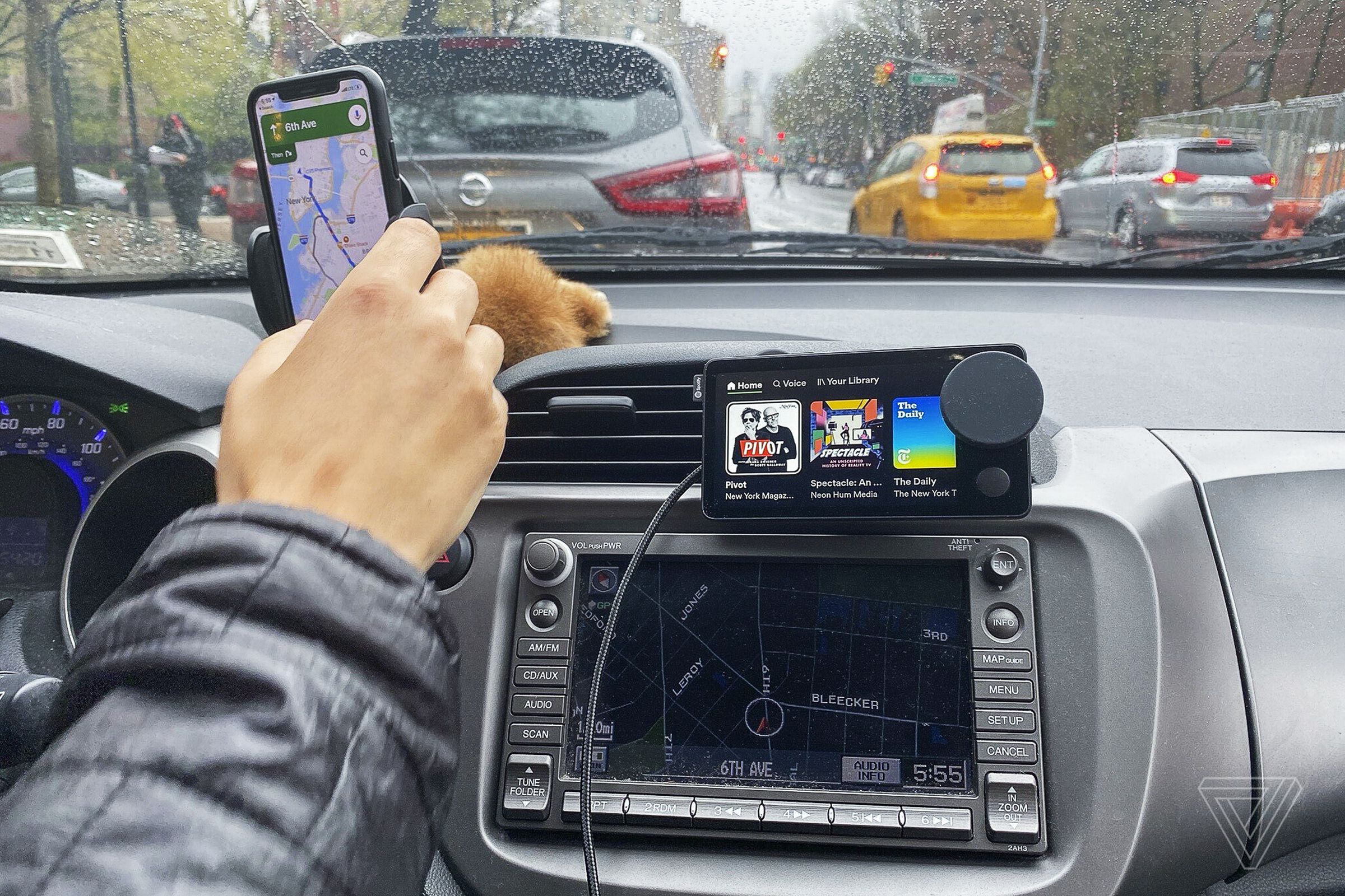 Seorang pengemudi di dalam mobil menggunakan Spotify Car Thing dan ponsel cerdas yang terpasang di dasbor.