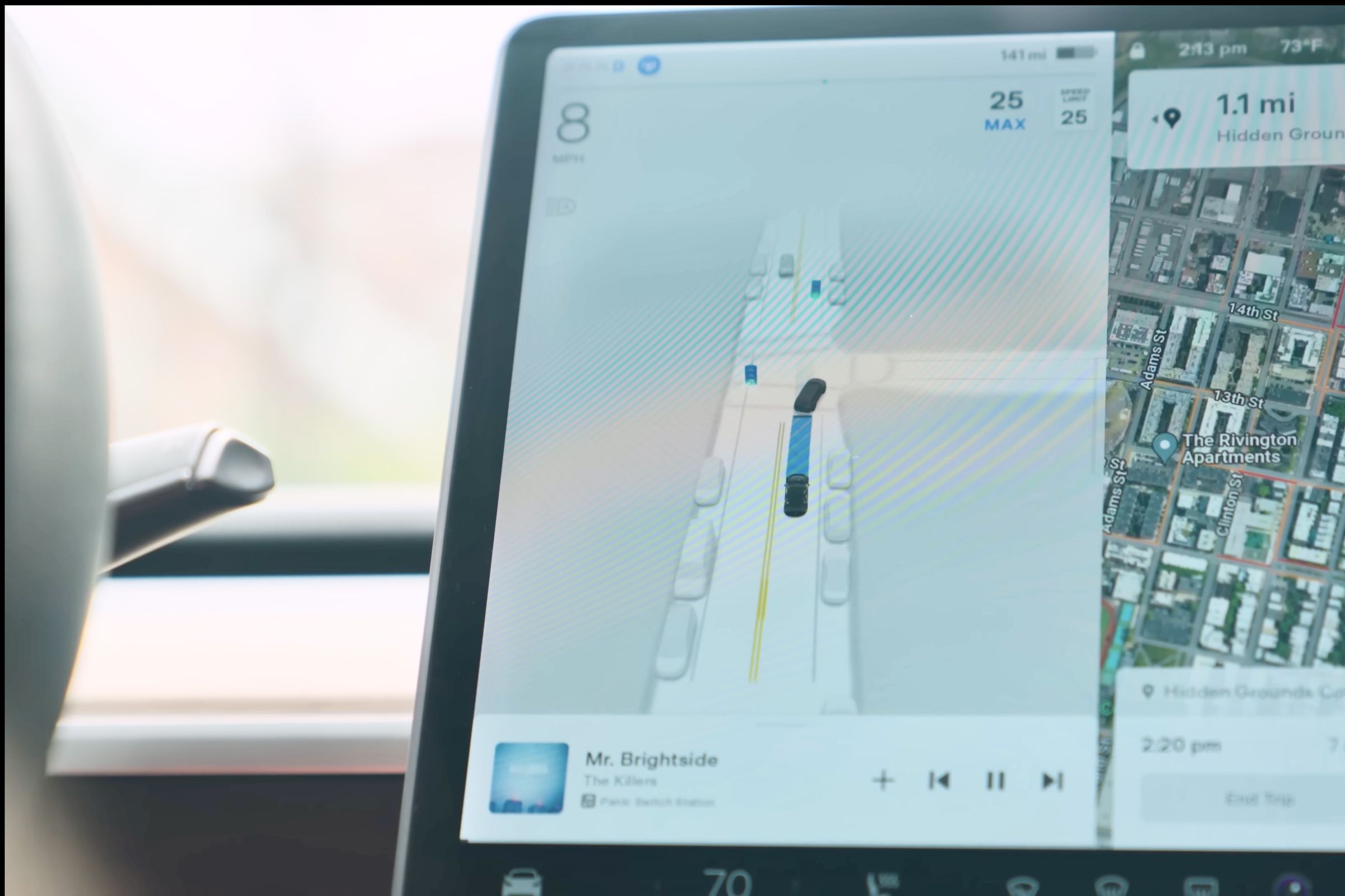 Bagian kiri layar utama Tesla Model 3 yang menampilkan gambar hasil komputer dari persimpangan jalan dengan mobil-mobil yang diparkir di sisi-sisinya dan Model 3 yang mengikuti mobil lain