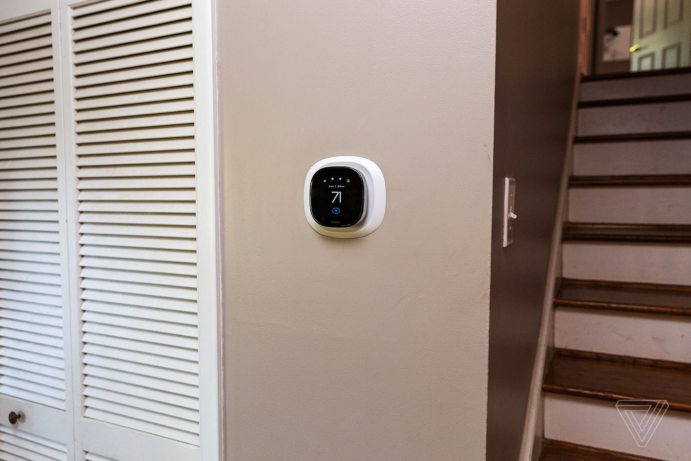 Termostat Ecobee berukuran kecil di dinding cokelat muda, terletak di antara lemari dan tangga.
